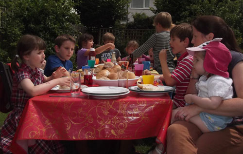 Children eating BBQ food at a table in the sunshine.