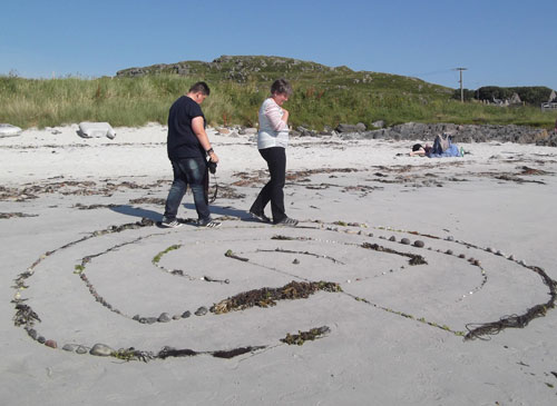 Two women walking aroung a labyrinth on the white sandy beach of Iona.