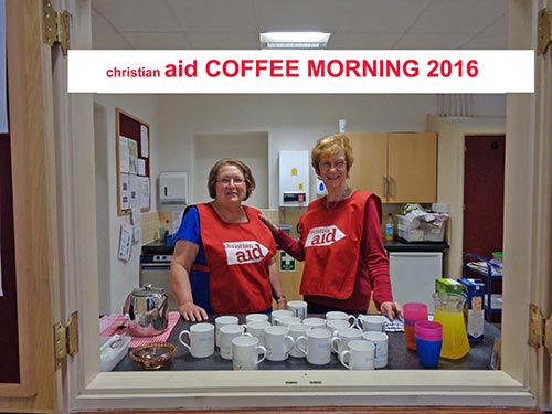 Image of Sue and Jenny at the serving hatch with Christian Aid aprons on.